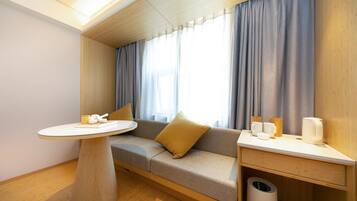 A modern room with a sofa, a round table, and a small desk with cups and a trash bin.