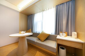 A modern room with a sofa, a round table, and a small desk with cups and a trash bin. - Ji Hotel (Nanjing)