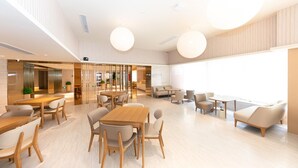 A spacious indoor area with a large wooden table surrounded by chairs, a seating area with sofas, and a large window providing natural light. - Ji Hotel (Nanjing)