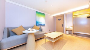 A modern hotel room with a grey sofa, a round coffee table, a wooden floor, a painting on the wall, and a wooden wardrobe. - Ji Hotel (Nanjing)