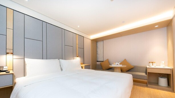 A hotel room with a large bed, bedside tables, a small table with a lamp, and a sofa. - Ji Hotel (Nanjing)