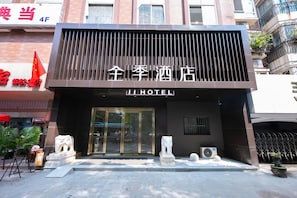 A hotel entrance with a modern facade, a lion statue, and a flag. - Ji Hotel (Nanjing)