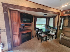 A compact RV interior with a dining area, a television, and a small kitchenette. - Cozy RV Rental at Sleepy Hollow Campgrounds (Gaines)