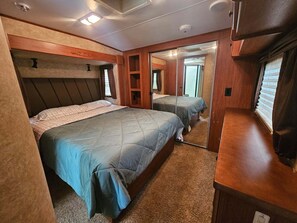 A bedroom with two beds, a wooden headboard, a mirror, and a small closet. - Cozy RV Rental at Sleepy Hollow Campgrounds (Gaines)
