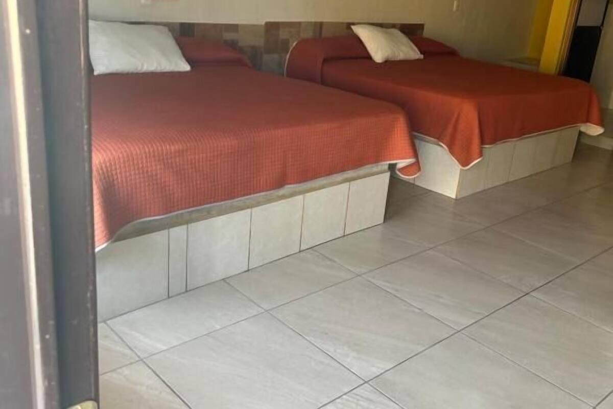 Habitación de hotel con dos camas, piso de baldosas y una puerta con picaporte.