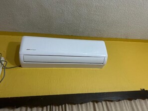 A white air conditioning unit mounted on a yellow wall.