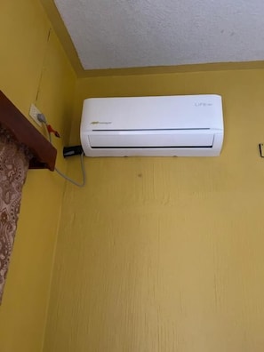 A white wall-mounted air conditioner on a yellow wall.