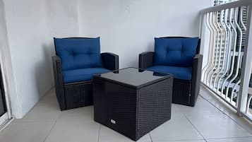 A balcony with two blue cushioned chairs and a black square table.