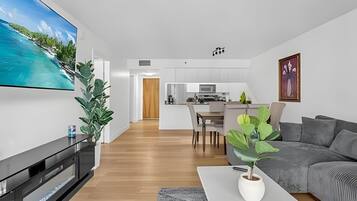 A modern living room with a flat-screen TV, a grey sofa, a coffee table, and a potted plant.