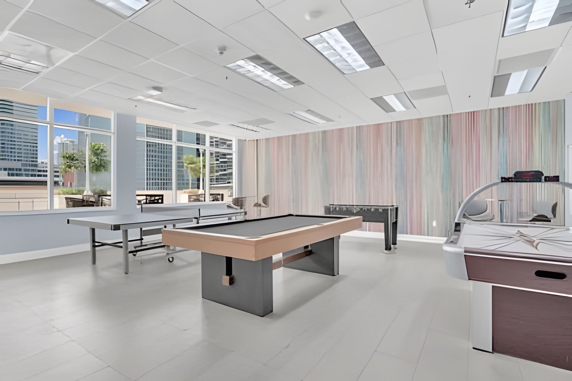 Uma área de lazer moderna em ambiente interno, com mesa de bilhar, mesa de futebol e mesa de ping pong.