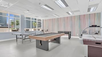 Uma área de lazer moderna em ambiente interno, com mesa de bilhar, mesa de futebol e mesa de ping pong.