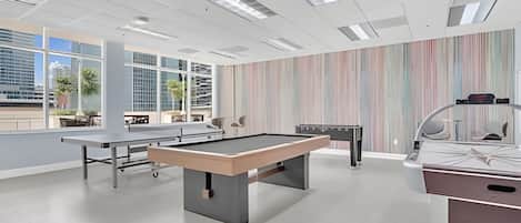 Un área recreativa moderna en interior con mesa de billar, mesa de futbolín y mesa de ping pong.