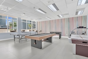 Un área recreativa moderna en interior con mesa de billar, mesa de futbolín y mesa de ping pong.