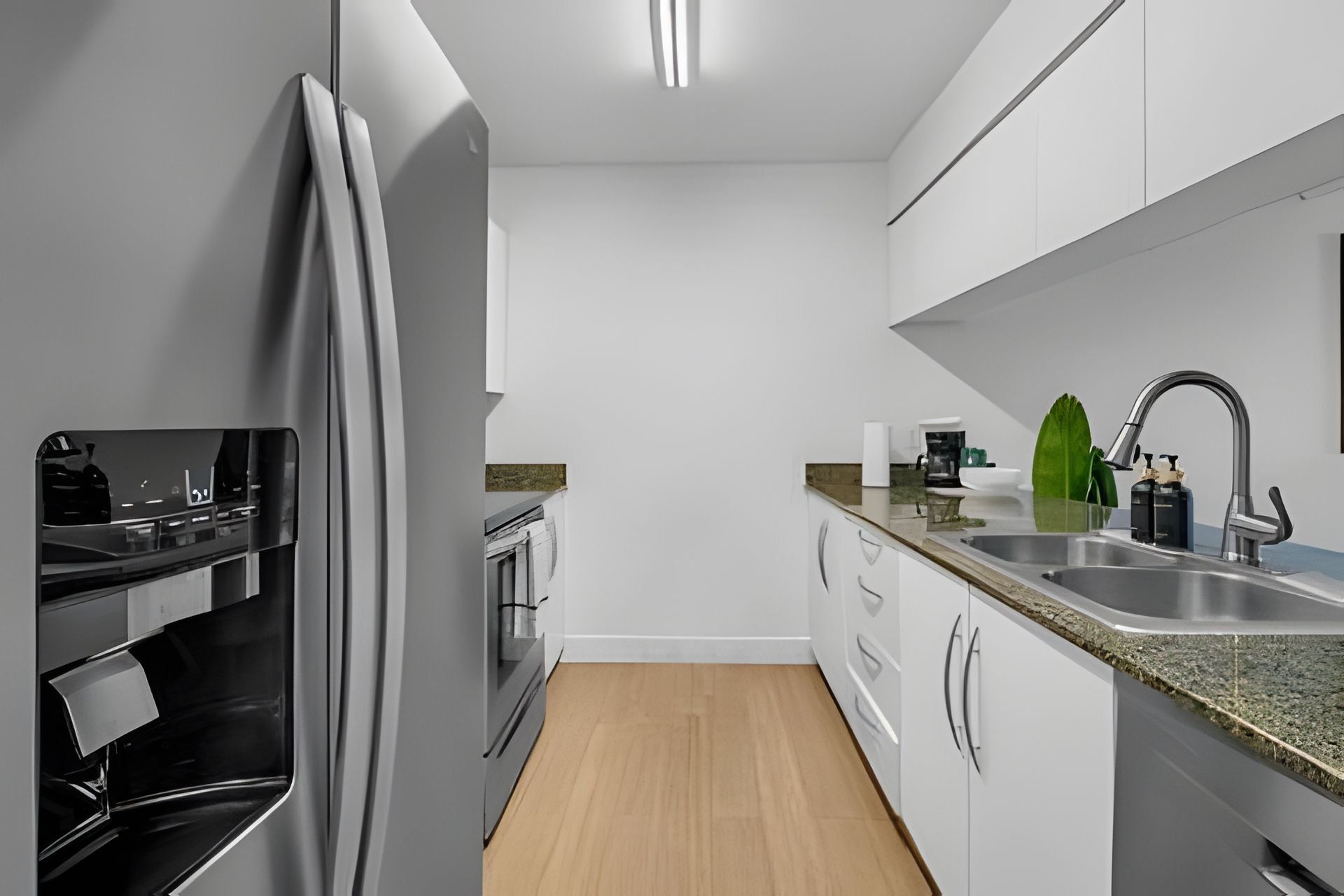 A modern kitchen with white cabinets, a stainless steel sink, and a built-in oven.