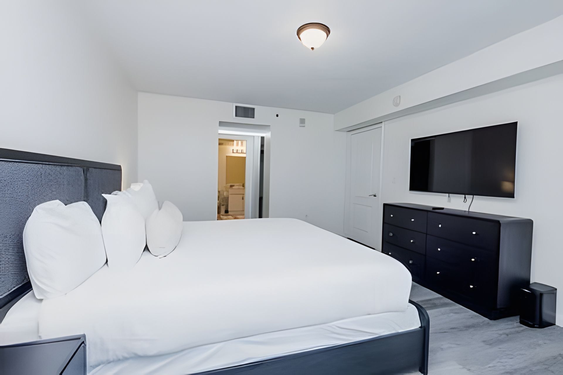 A modern bedroom with a large bed, a flat-screen TV, and a walk-in closet.