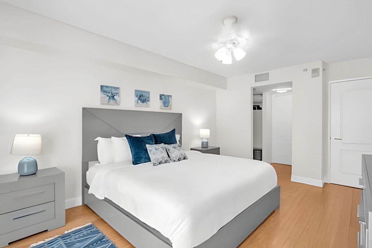 Un dormitorio moderno con una cama grande, mesitas de noche, un ventilador de techo y una obra de arte en la pared.