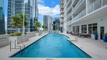 A swimming pool with a view of high-rise buildings, a covered seating area, and a clear sky.