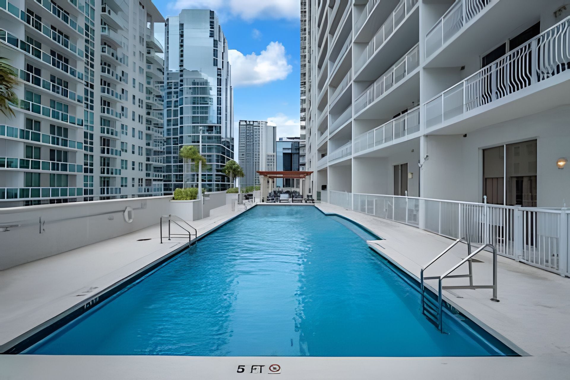 A swimming pool with a view of high-rise buildings, surrounded by a white balcony with railings.