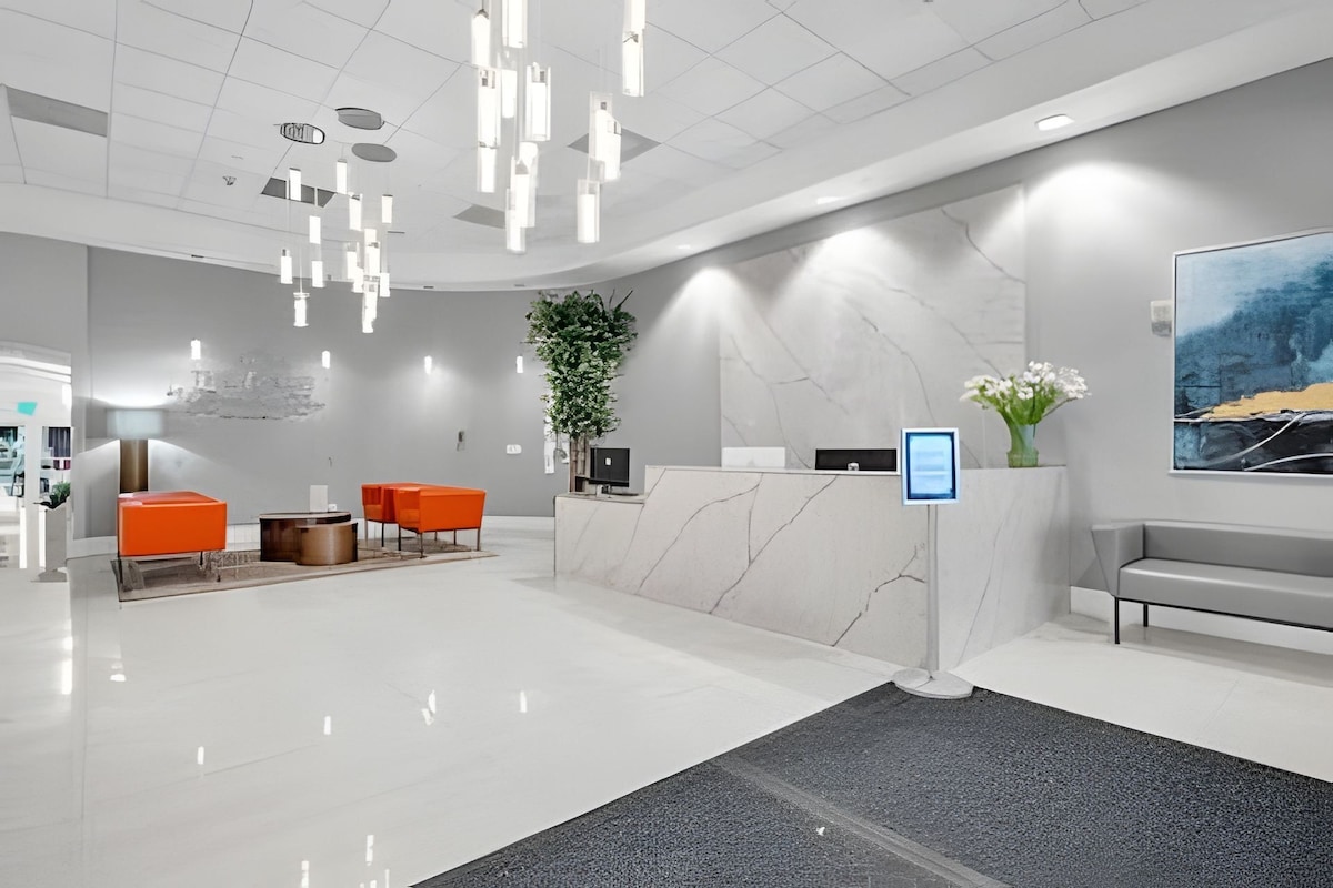 Uma área de recepção moderna com balcão de mármore, um quiosque digital e assentos.