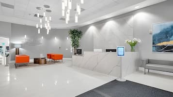 Uma área de recepção moderna com balcão de mármore, um quiosque digital e assentos.