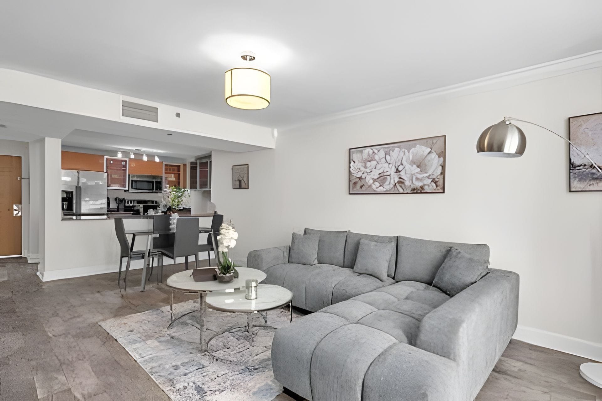 A modern living room with a grey sectional sofa, a coffee table, and a dining area with chairs.