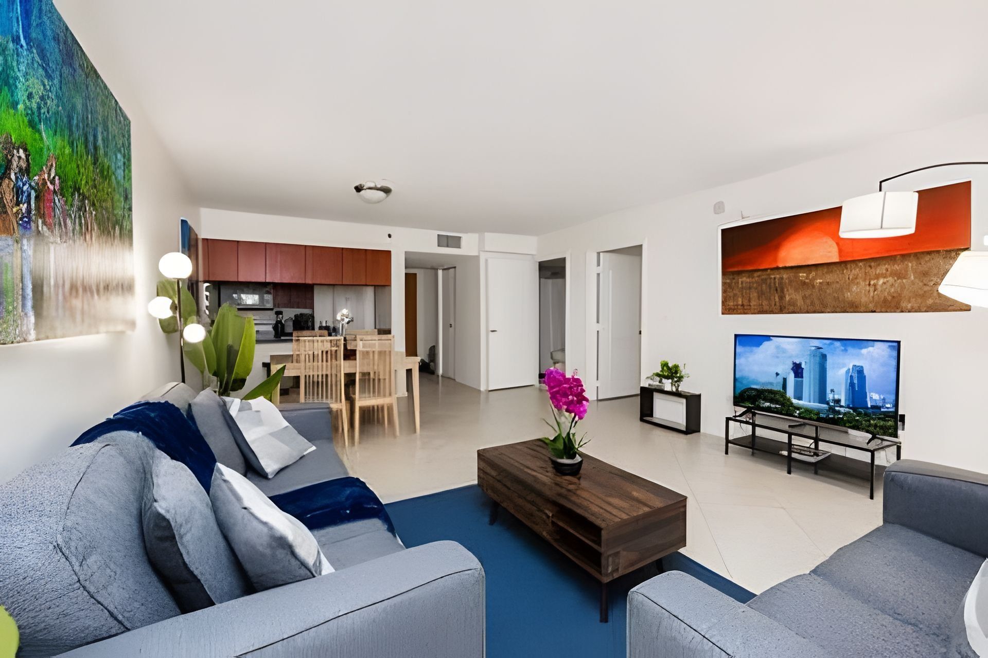 A modern living room with a grey sofa, a coffee table with a plant, and a television on the right.
