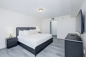Un dormitorio moderno con cama, mesitas de noche, un televisor de pantalla plana y una puerta que da a otra habitación.