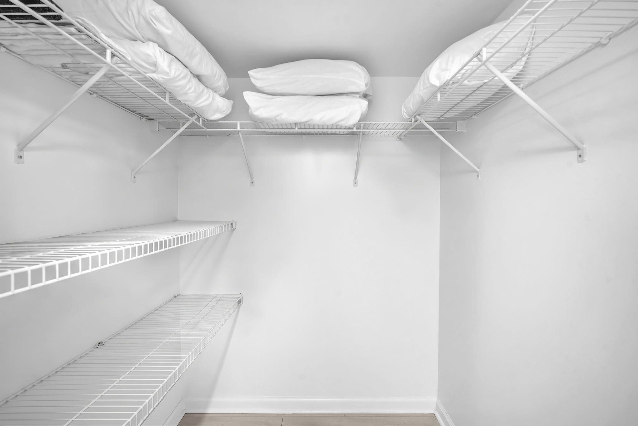 Un placard blanc avec trois étagères en fil métallique et deux espaces pour suspendre des vêtements, offrant ainsi un espace de rangement.