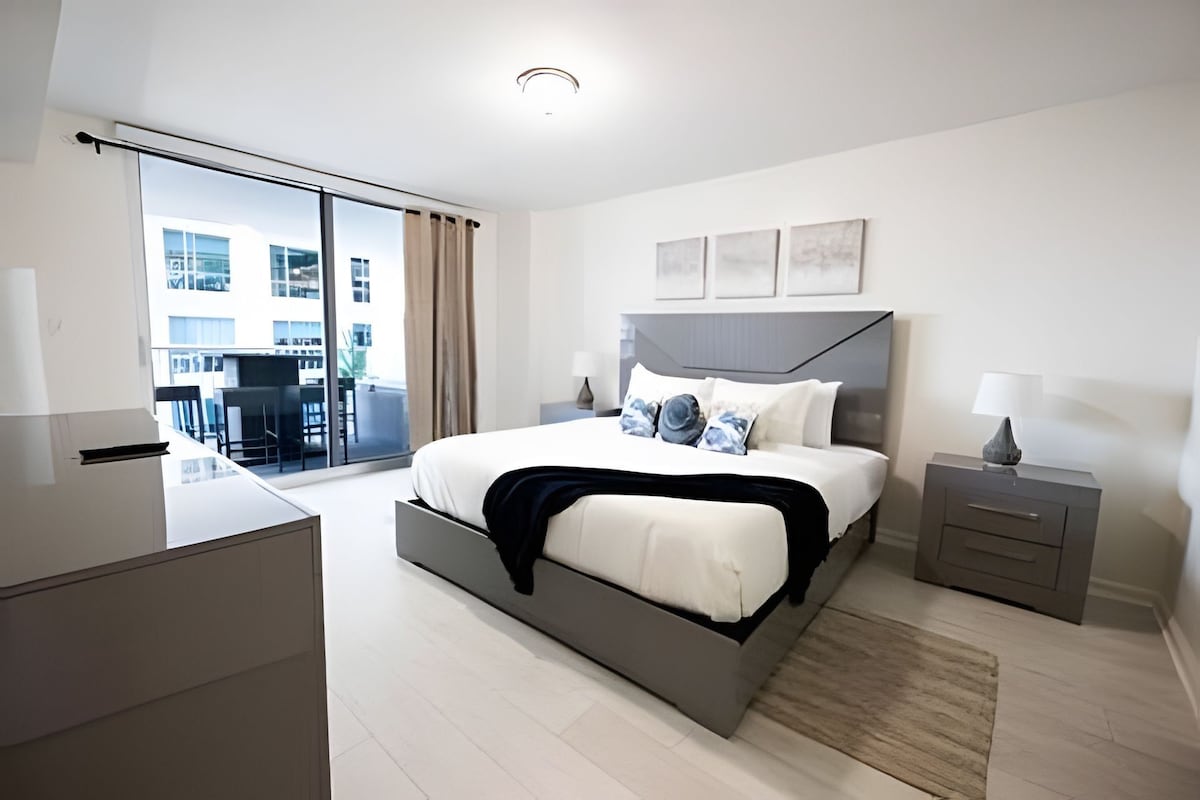 Quarto de hotel moderno com uma cama grande, uma escrivaninha e vista para a cidade.
