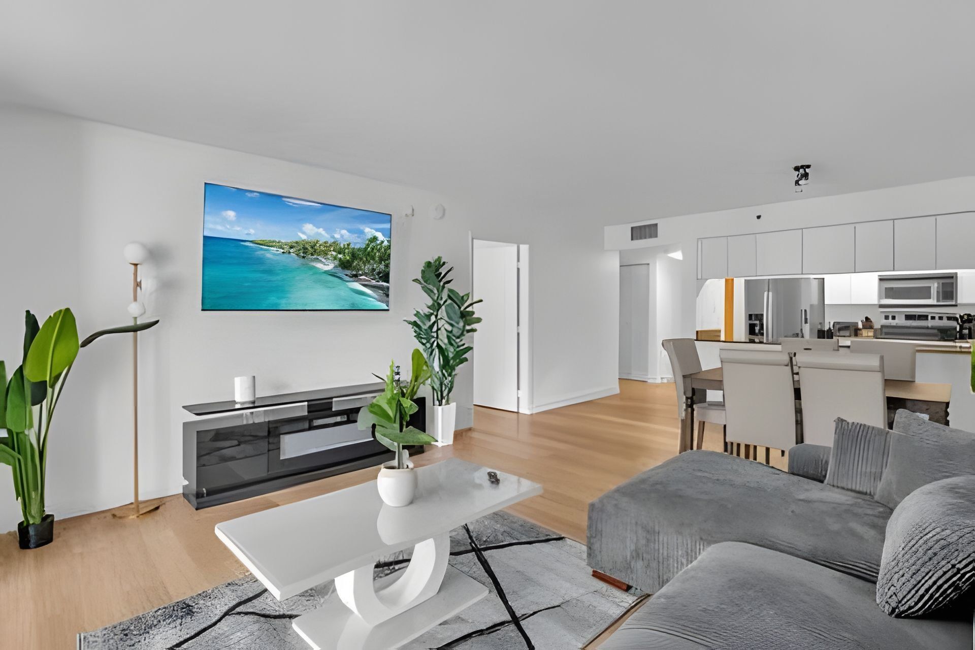 A modern living room with a flat-screen TV, a sofa, a coffee table, and a kitchen in the background.