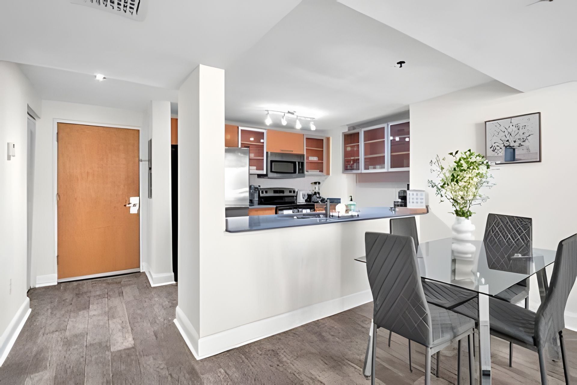 A modern kitchen with a central island, white cabinetry, and a dining area with a glass table and chairs.