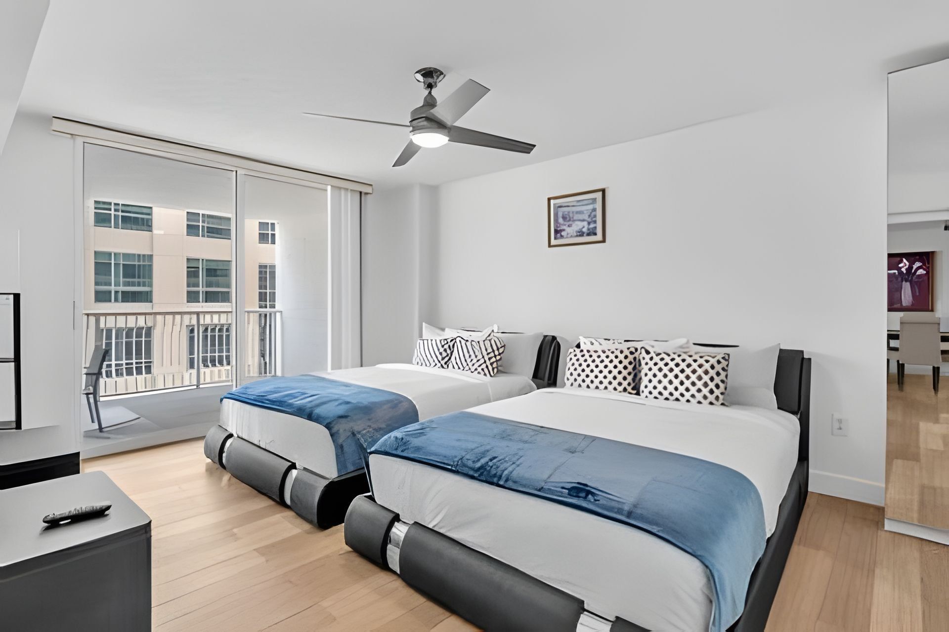 Ein modernes Schlafzimmer mit zwei Betten, einem Deckenventilator und einem großen Fenster.
