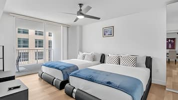 A modern bedroom with two beds, a ceiling fan, and a large window.