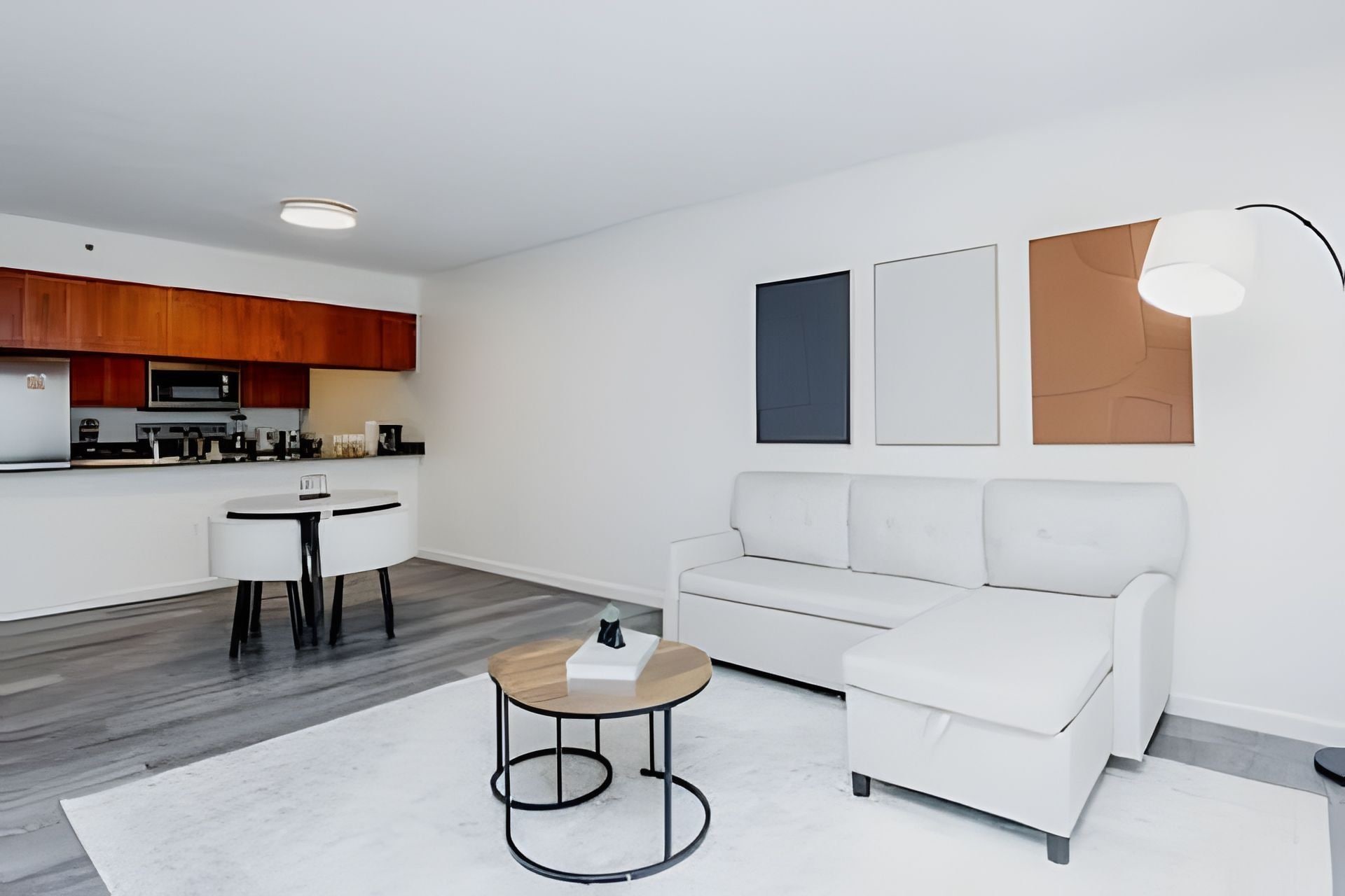 A modern living room with a white sofa, a round coffee table, and a kitchen area with wooden cabinets and a microwave.