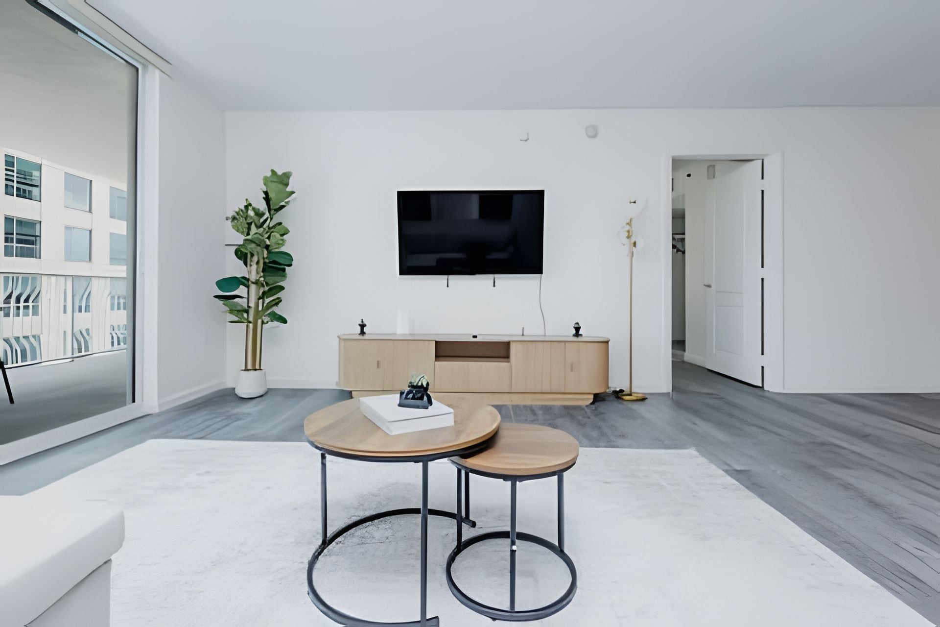 Un salon moderne avec une grande fenêtre, un téléviseur à écran plat, un meuble en bois et une plante en pot.