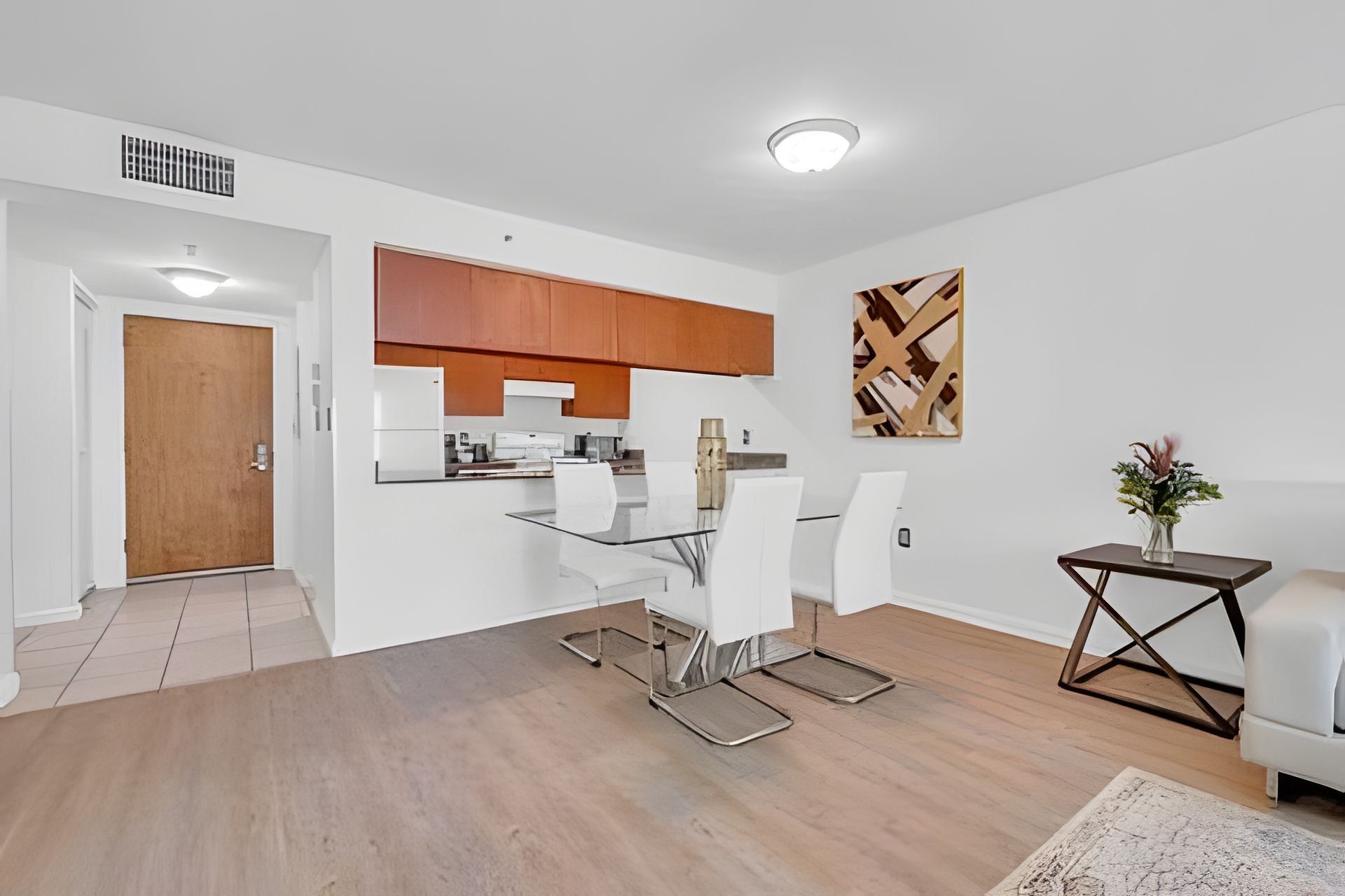 A modern kitchen with white cabinets, a dining area with a glass table and white chairs, and a living area with a sofa and a small side table.