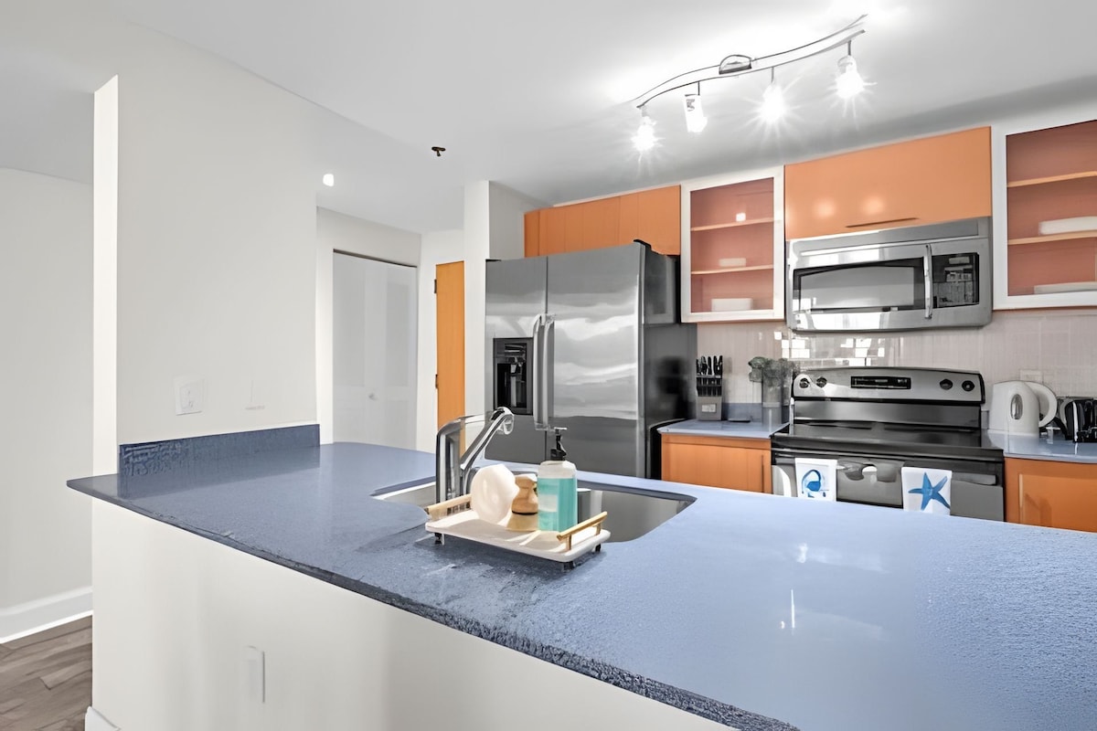 Cozinha moderna com ilha central, eletrodomésticos de aço inoxidável e bancada azul.