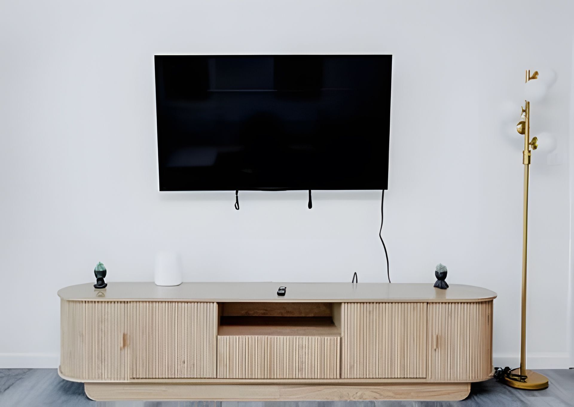 A modern entertainment unit with a flat-screen TV mounted on the wall, a wooden cabinet with a built-in shelf, and a floor lamp beside it.