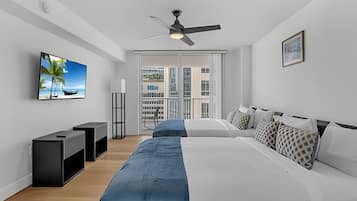 A modern bedroom with a large bed, a TV, a ceiling fan, and a view of the city through the window.