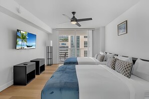 Un dormitorio moderno con una cama grande, un televisor, un ventilador de techo y vistas a la ciudad desde la ventana.