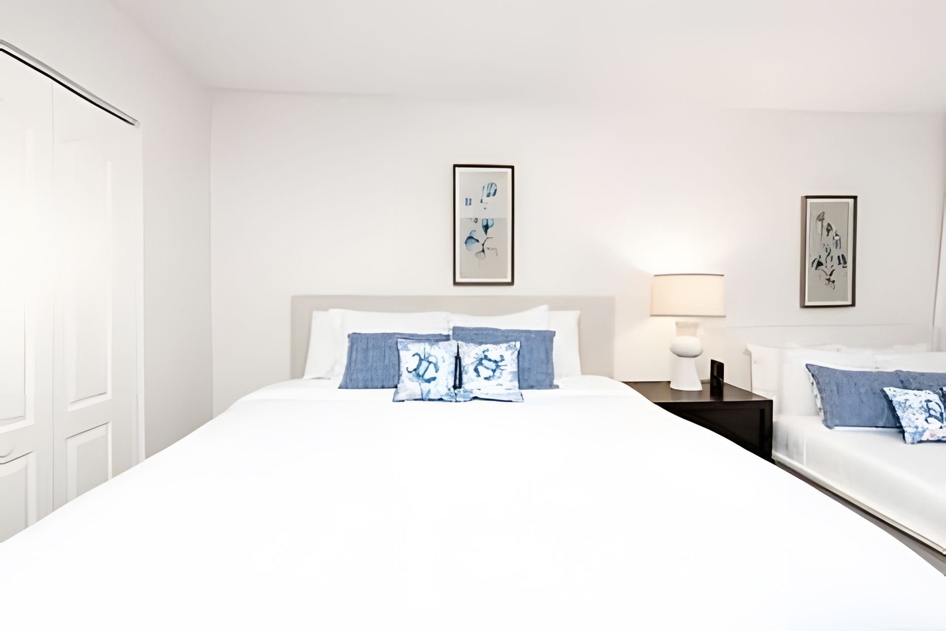Een hotelkamer met een groot bed, twee nachtkastjes en twee ingelijste kunstwerken aan de muur.