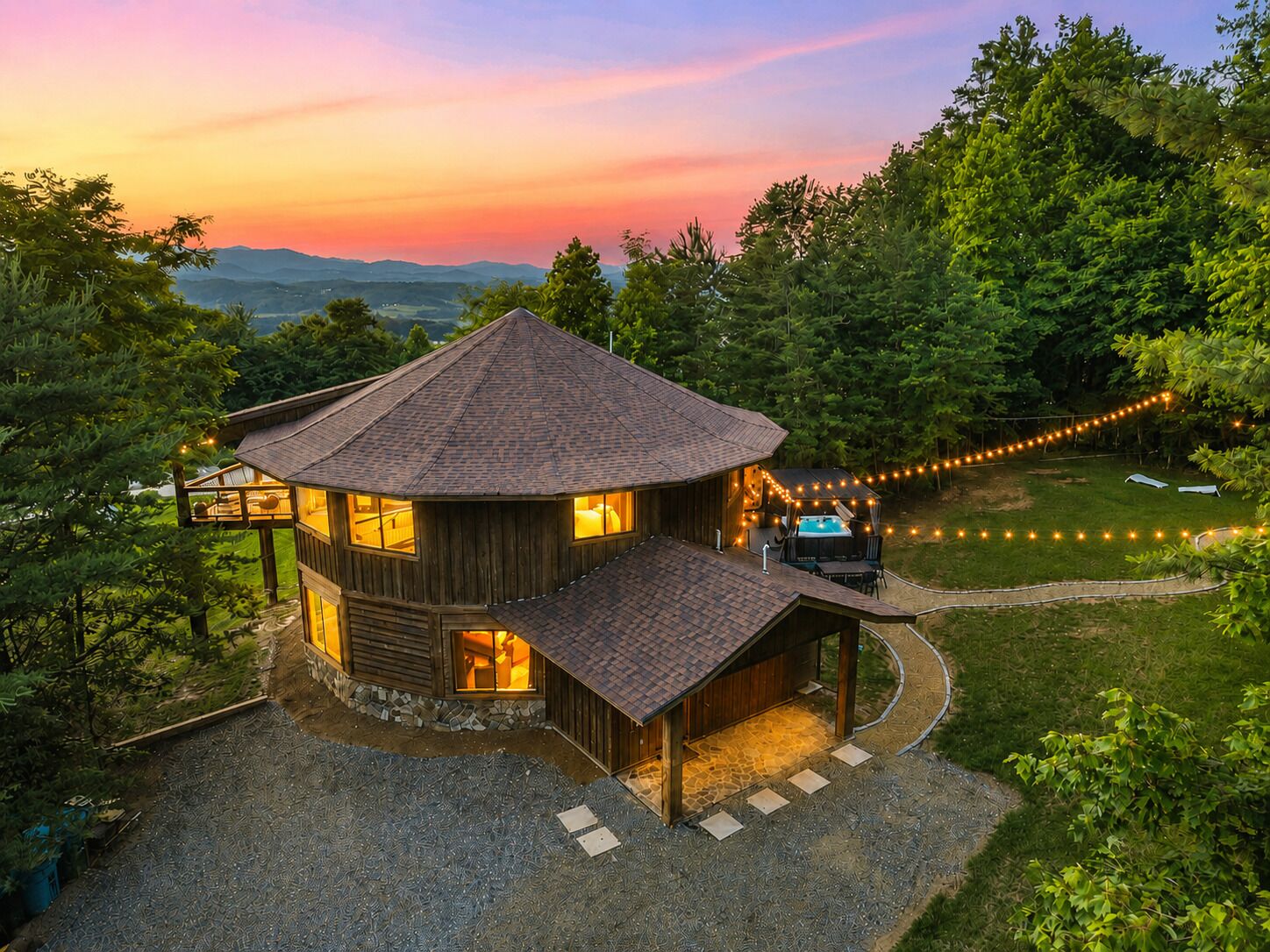 A wooden cabin with a curved roof, a hot tub, and string lights in a forested area.