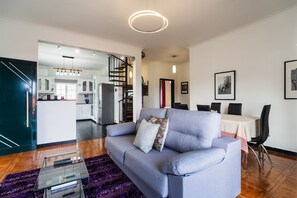 A modern living room with a sofa, a glass coffee table, and a dining area with chairs and a table. - GuestReady - Charming coastal getaway in Caniço (Caniço)