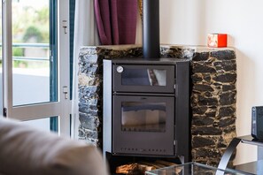 A wood-burning stove with a stone wall and a window. - GuestReady - Charming coastal getaway in Caniço (Caniço)