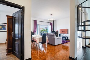 A modern living room with a sofa, dining table, and chairs, a TV, and a balcony with a view. - GuestReady - Charming coastal getaway in Caniço (Caniço)