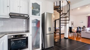 Een moderne keuken met een inbouwoven, een roestvrijstalen koelkast en een spiltrap die naar een eethoek leidt.