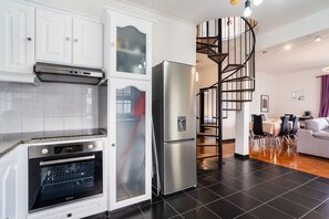 A modern kitchen with a built-in oven, a stainless steel refrigerator, and a spiral staircase leading to a dining area. - GuestReady - Charming coastal getaway in Caniço (Caniço)