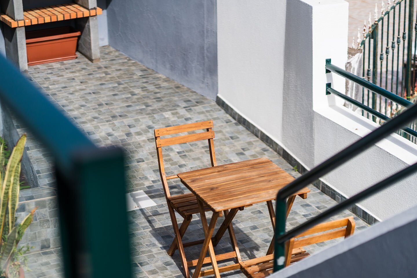 A wooden table and chairs on a tiled balcony with a view of a building and a metal railing.