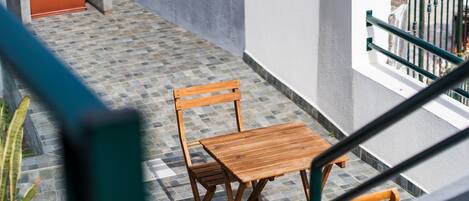 A wooden table and chairs on a tiled balcony with a view of a building and a metal railing.