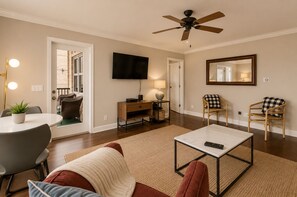 A living room with a ceiling fan, a flat-screen TV, a dining table with chairs, a sofa, and a coffee table.